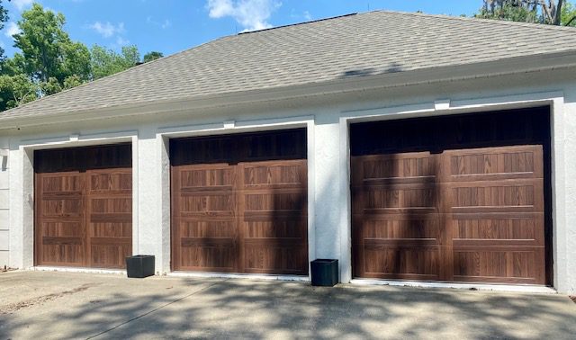 Two wooden garage doors on a white house under sunlight.